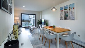 A modern dining area with a wooden table and white chairs, a TV, and a view through a glass door to an outdoor patio. - Alcaidesa Golf and Beach 2356 (La Alcaidesa)