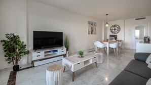 A modern living room with a flat-screen TV, a dining area with a table and chairs, and a grey sofa. - Alcaidesa Golf and Beach 2356 (La Alcaidesa)