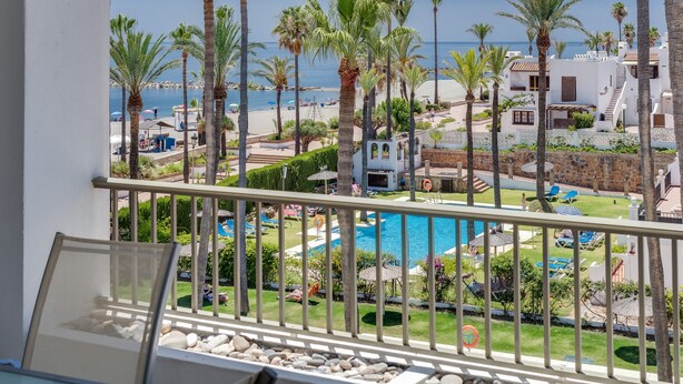 A balcony with a view of a pool, palm trees, and a beach.