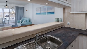 A modern kitchen with a large island, stainless steel sink, and a dining area with a blue sofa and table.