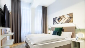 Een moderne hotelkamer met een groot bed, een flatscreen televisie aan de muur en een schilderij boven het bed.
