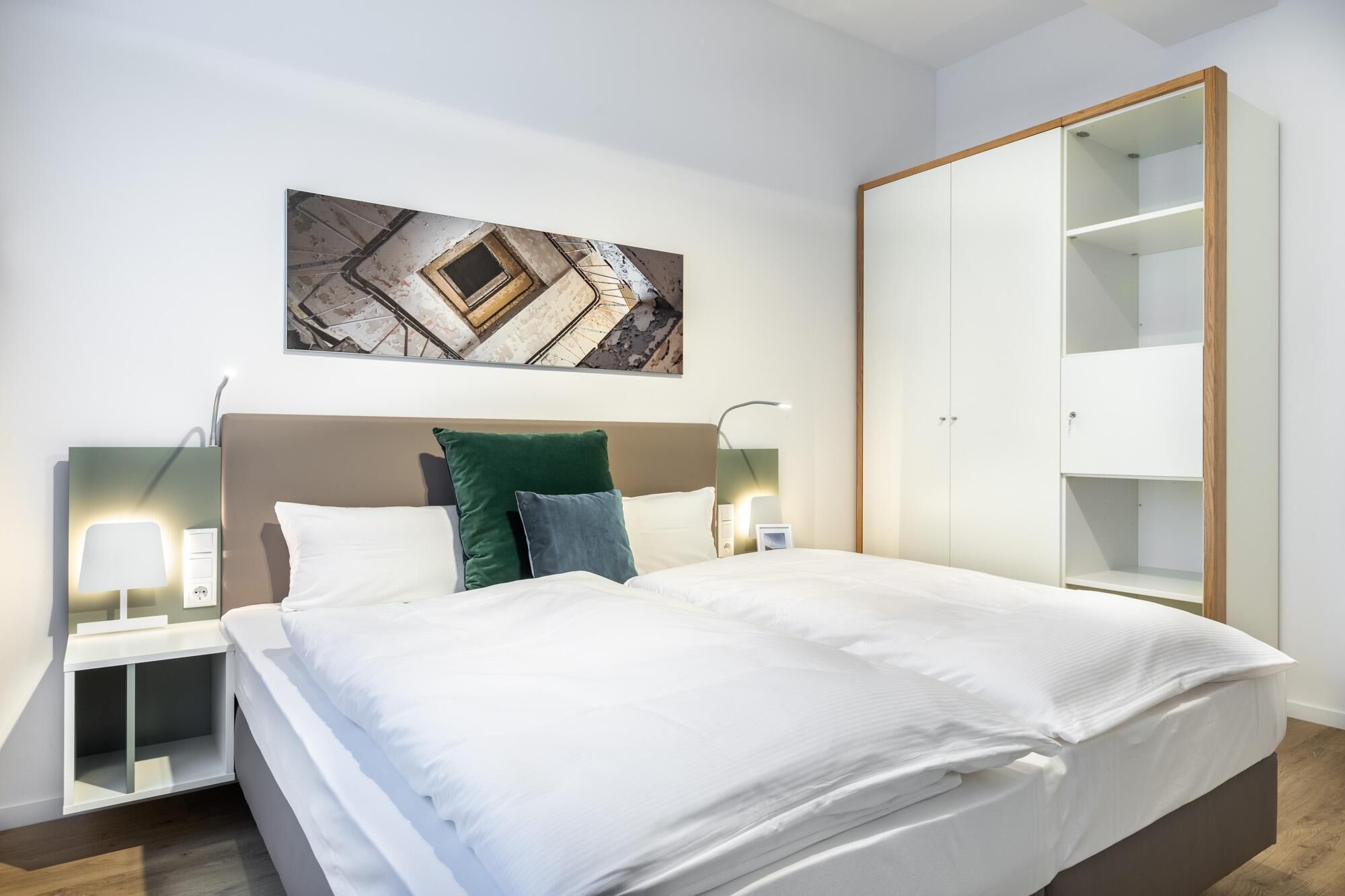 Ein modernes Schlafzimmer mit einem großen Bett, einem Nachttisch mit Lampe, einem Kleiderschrank und einem Wandbild.
