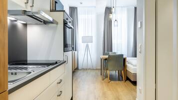 A compact kitchen with modern appliances, a dining area with a table and chairs, and a bed in the background.