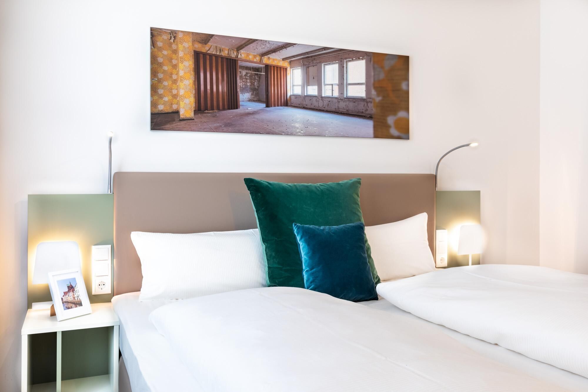 Habitación de hotel con una cama grande, dos mesitas de noche, un cabecero y un cuadro colgado en la pared.