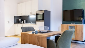 A modern kitchen with white cabinets, a built-in oven, and a coffee machine. There is a dining area with a wooden table and two chairs.