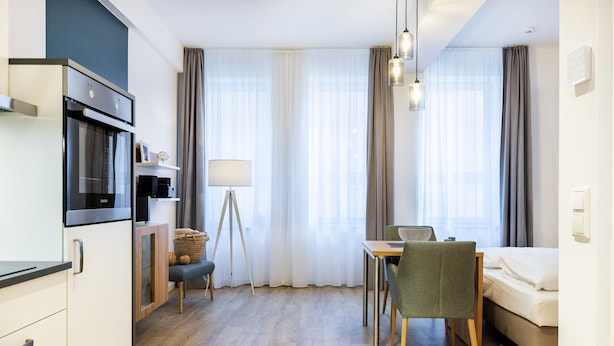 A modern hotel room with a kitchenette, a dining area, and a bed.