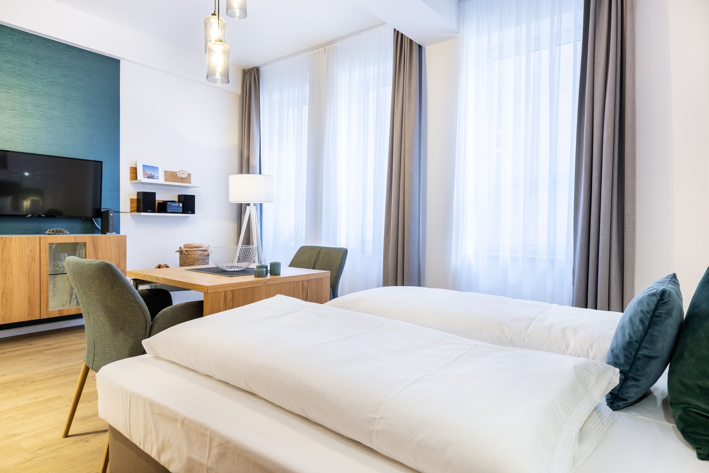 A hotel room with a bed, a desk with a lamp, a TV, and a view of the outdoors.