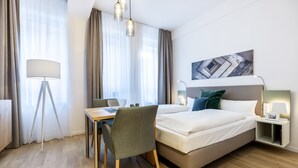 Habitación de hotel con cama, escritorio, silla, lámpara y un cuadro en la pared.