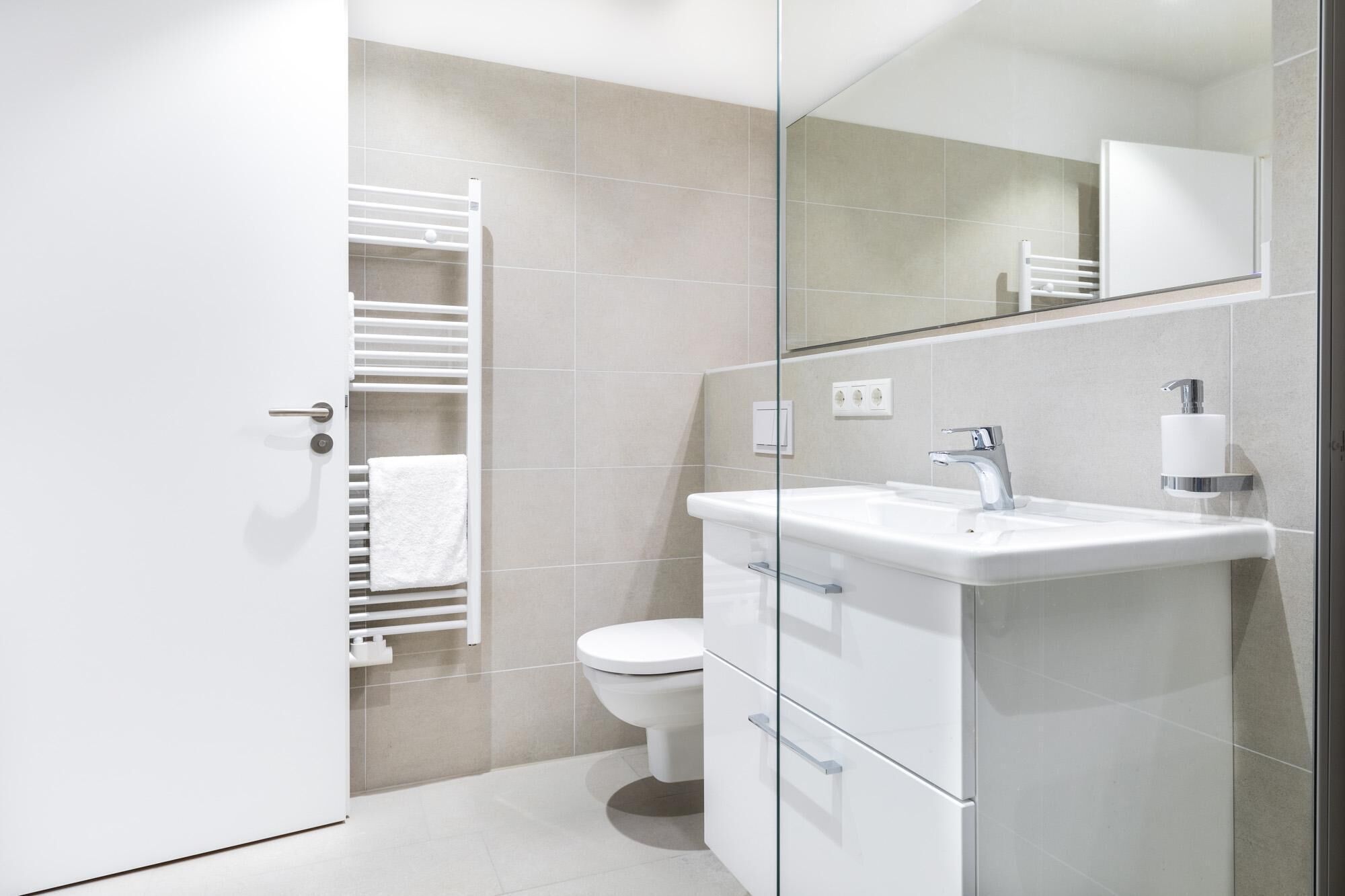 Een moderne badkamer met een douchecabine van glas, een wit wastafelmeubel met een chromen kraan, en een toilet.