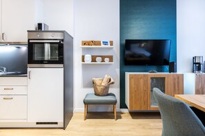 A modern kitchen with a built-in oven, a television, and a dining area with a wooden table and a chair.