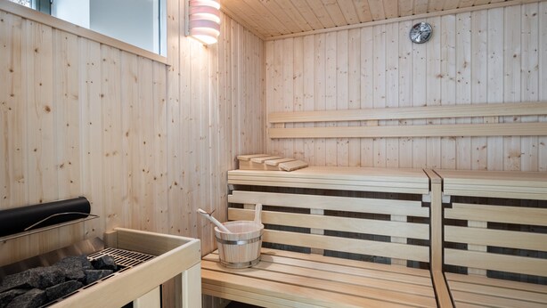 Una sauna con bancos de madera, un balde y una parrilla.