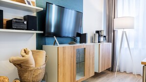 A modern hotel room with a flat-screen TV, a coffee machine, a wicker basket with a blanket, and a wooden cabinet.