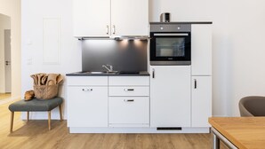 Una cocina compacta con armarios blancos, horno integrado y un lavamanos.