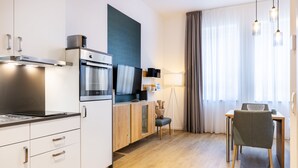A modern kitchen with a built-in oven, a microwave, and a coffee machine. There is a dining area with a table and chairs, and a large window with curtains. - Modernes, Hundefreundliches Apartment in Außergewöhnlicher Hafenlage von Wismar (Hansestadt Wismar)