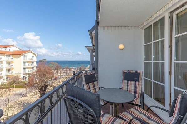 A balcony with a round table and chairs, overlooking a beach and ocean.