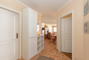 A hallway with white doors, a kitchen area with cabinets and a dining table.