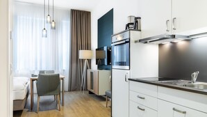 Una cocina moderna con horno empotrado, microondas y cafetera. Cuenta con un comedor con mesa y sillas, y una lámpara.