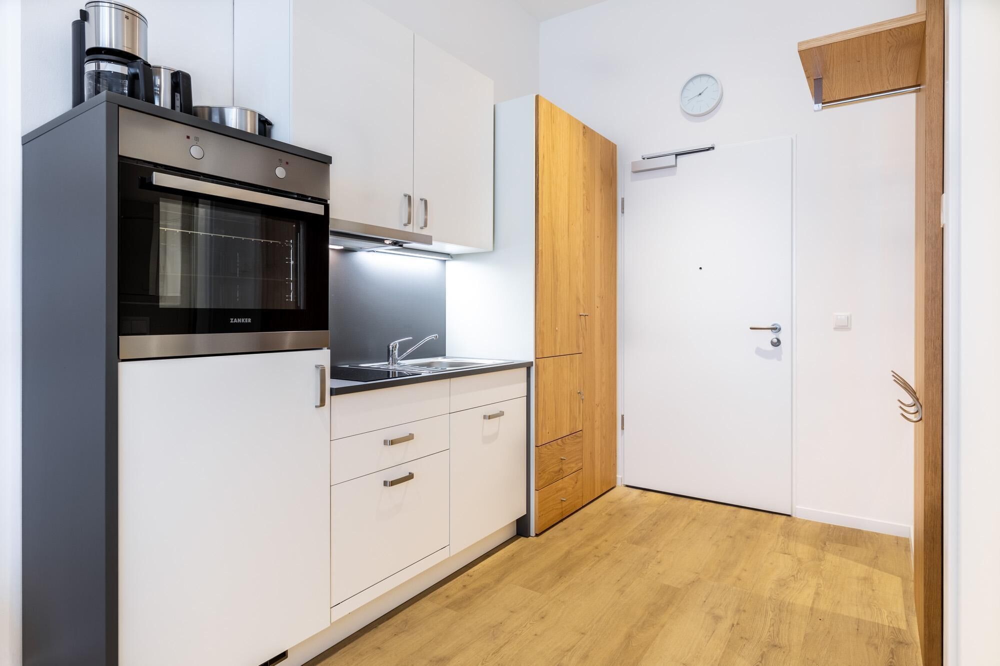 A modern kitchen with white cabinetry, a stainless steel oven, and a wooden door.