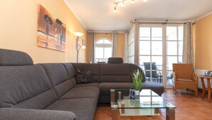 A living room with a grey sofa, a glass coffee table, a wicker chair, and a painting on the wall.