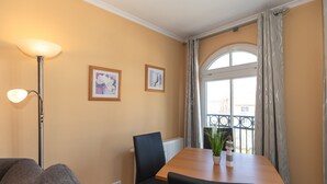 A room with a wooden table, two black chairs, a floor lamp, and two framed pictures on the wall.