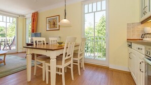 A dining area with a wooden table and white chairs, a hanging light fixture, and a view through large windows.