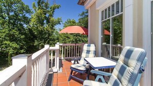 A patio with a table and chairs, a red umbrella, and a view of trees.