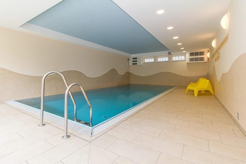 An indoor swimming pool with a blue ceiling, tiled floor, and a yellow chair near the pool.