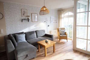 Ein modernes Wohnzimmer mit einem grauen Ecksofa, einem Holztisch und einem Korbstuhl.