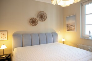 Ein Schlafzimmer mit einem Bett, zwei Wanddekorationen, einem gerahmten Bild, einer Lampe und einem Fenster mit Blick.