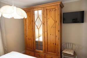 A bedroom with a wooden wardrobe, a bed, a chair, and a television on the wall.