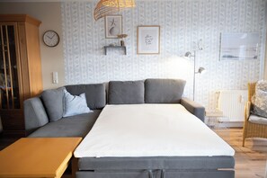 A bedroom with a large bed, a sofa, a wooden cabinet, and a wicker chair.