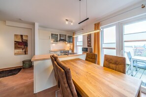Una cocina moderna con armarios blancos, una isla de madera y un comedor con mesa y sillas de madera.