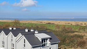 A two-story house with a dark roof and white trim, overlooking a coastal landscape with a lighthouse in the distance.