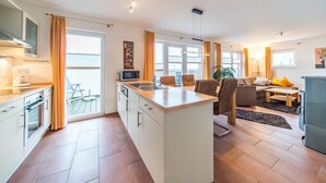 A modern apartment with a kitchen, dining area, and living room. It features a large island in the kitchen, a dining table with chairs, and a sofa in the living room.