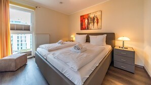 A hotel room with a large bed, two bedside tables, a window with curtains, and a painting on the wall.