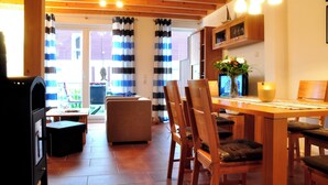A cozy dining area with a wooden table and chairs, a sofa, and a kitchen in the background. - Great vacation home on the dyke with terrace, balcony with sea view, sauna & wood-burning stove (Nordseeheilbad Schillig)