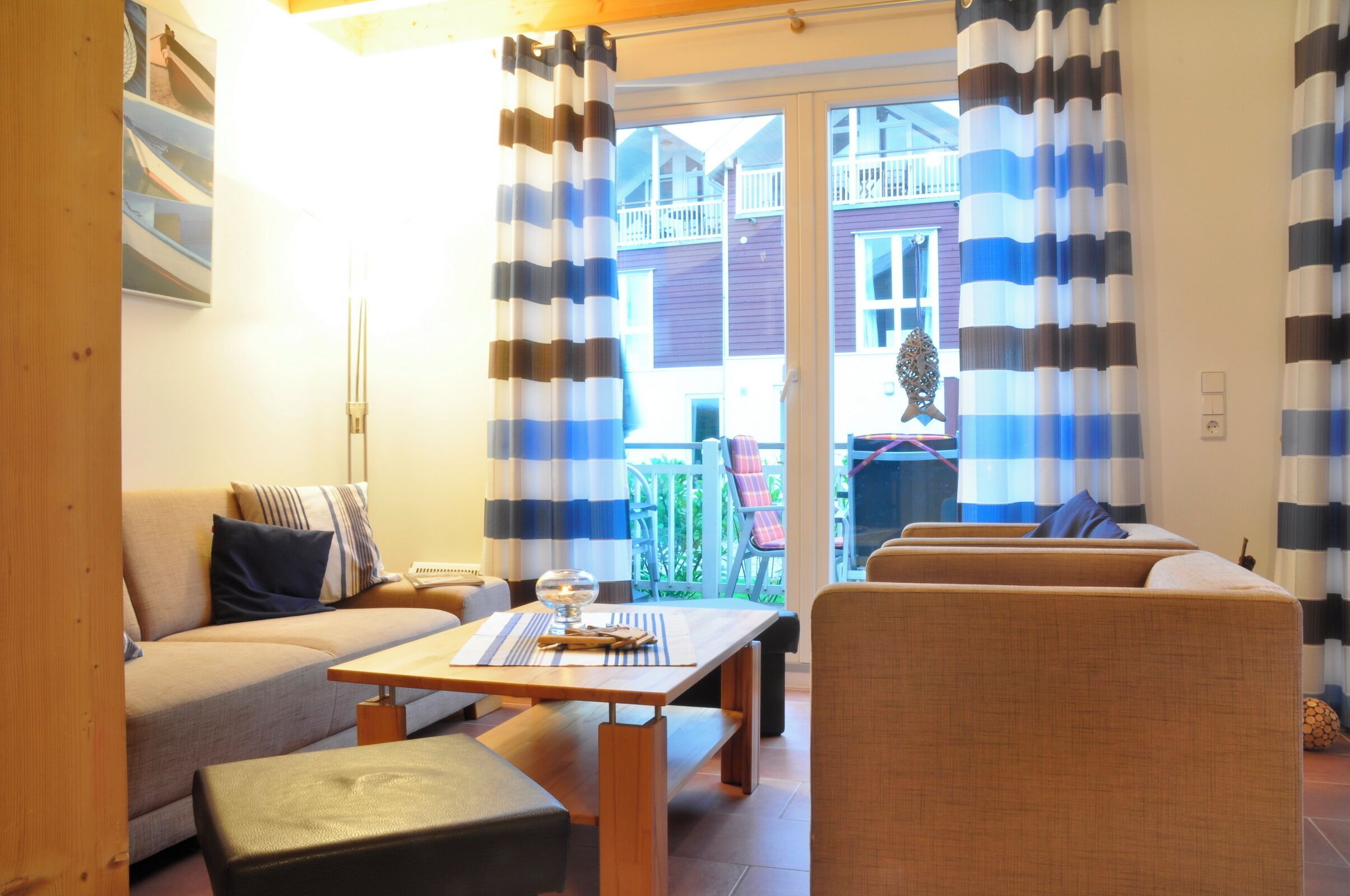A cozy living area with a sofa, a table, and a bench. There is a window with curtains, and a balcony with a railing and chairs.