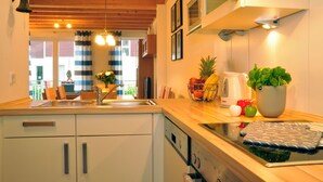 A kitchen with wooden cabinets, a sink, a stove, and a countertop with fruits and a plant. - Great vacation home on the dyke with terrace, balcony with sea view, sauna & wood-burning stove (Nordseeheilbad Schillig)