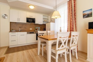 A modern kitchen with white cabinets, a wooden countertop, and a dining area with a wooden table and white chairs.