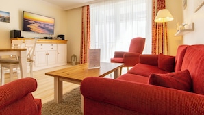 A living room with a red sofa, a wooden coffee table, and a TV on the wall.