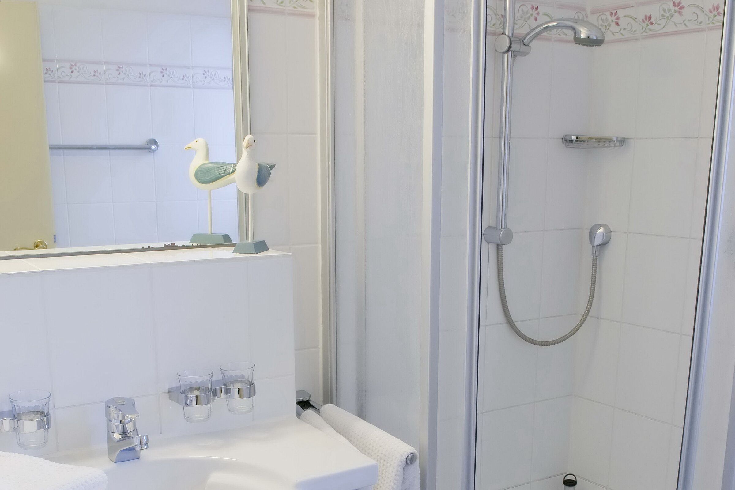 A bathroom with a white sink, two glass soap dispensers, a towel rack, and a shower with a handheld showerhead.