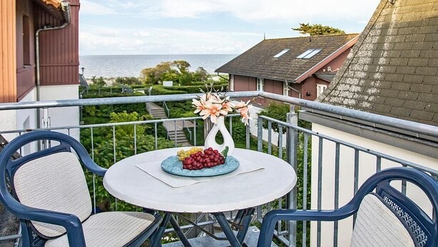 A balcony with a table, chairs, a vase with flowers, and a plate of grapes.