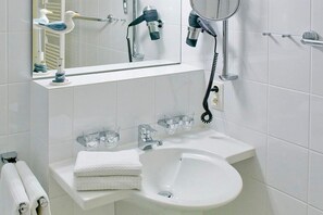 Ein Badezimmer mit einem weißen Waschbecken, zwei Wasserhähnen, einem Spiegel und einem an der Wand montierten Föhn.