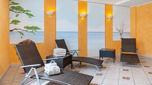 A spa area with reclining chairs, a massage table, and a view of the sea through a mural.