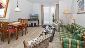 A living room with a dining table, chairs, a sofa, a TV, and a lamp.