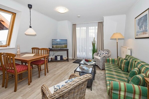 Ein Wohnzimmer mit Esstisch, Stühlen, einer Couch, einem Fernseher und einer Lampe.