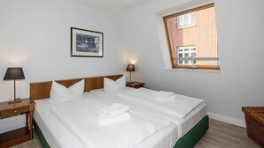 A hotel room with a large bed, two bedside tables, a framed picture on the wall, and a window with a view of a building.