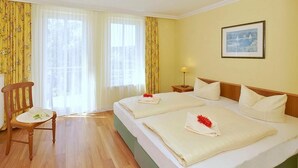 A hotel room with two beds, a wooden chair, a small table, and a picture on the wall.