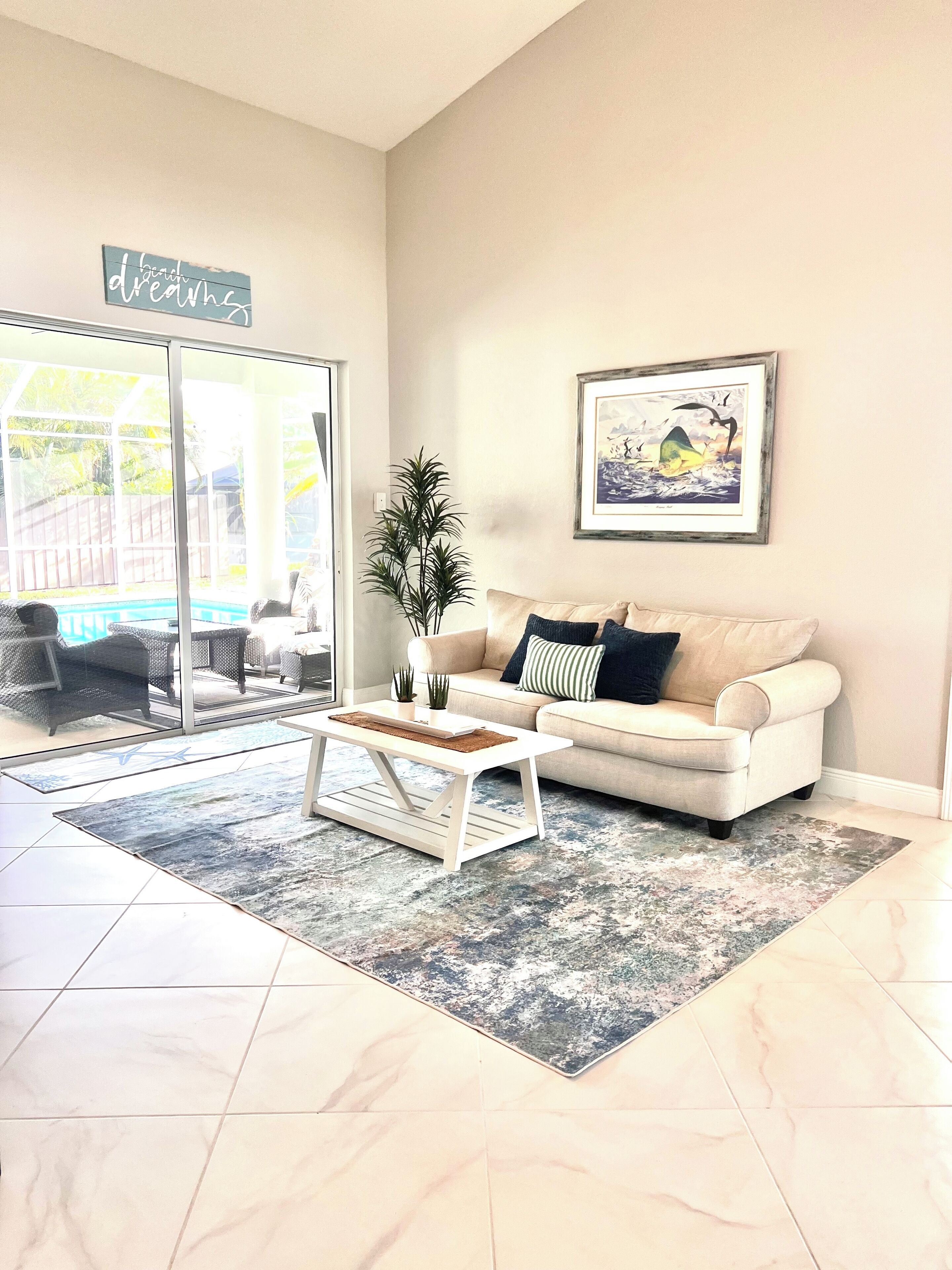 A living room with a beige sofa, a coffee table, a framed picture, and a potted plant.