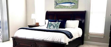 A spacious bedroom with a large bed, a headboard with a painting, and a view of the outside through a window.